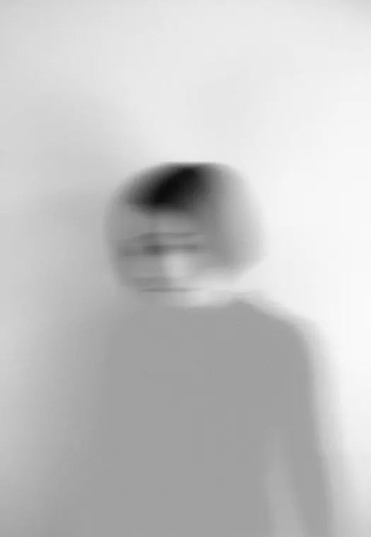 A woman standing in half light against a plain wall